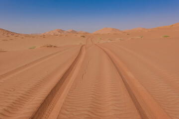 Fototapeta na wymiar Tyre tracks on red sand in the Rub al Khali desert in the background the dunes and a blue sky. Oman.