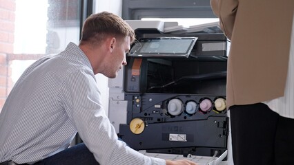 Photocopier or printer has error. Young businessman checking a photocopier machine in office....