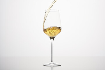 White alcohol beverage flows to wineglass, close up on white isolated.