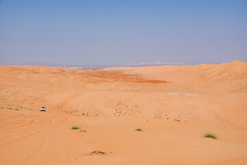 Wahiba sand orange desert on the horizon a white jeep. Oman.