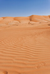 Fototapeta na wymiar Wavy orange sand imprint against a backdrop of sand dunes and blue sky.
