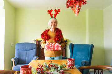 A joyful old woman, against the backdrop of a festive table, is preparing to give Christmas gifts to her family.