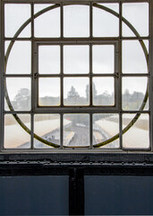 Round window, art deco design overlooking the train platform. Rain obscures the view.