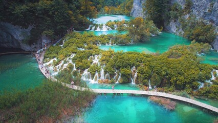People hiking on narrow bridge over crystal clear emerald green water of lakes. Tourists walking...
