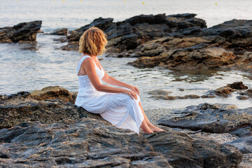 beautiful woman over 50 years old on the beach with a white dress