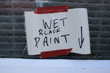 Hand written sign "Wet black paint" with arrow pointing down attached to a window with brown tape