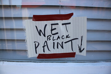 Hand written sign "Wet black paint" with arrow pointing down attached to a window with brown tape