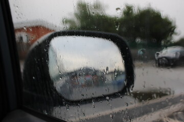 Rain on car window with blurred background car wing mirror and small car park