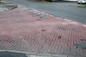 Patchy UK junction paved with red bricks and various potholes filled with tarmac
