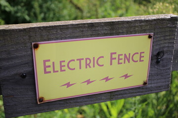 Yellow Electric Fence sign attached to a wooden fence, used to prevent animals from escaping their enclosure
