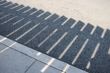 Fototapeta premium Detailed shadow of wooden fence on pavement and asphalt road