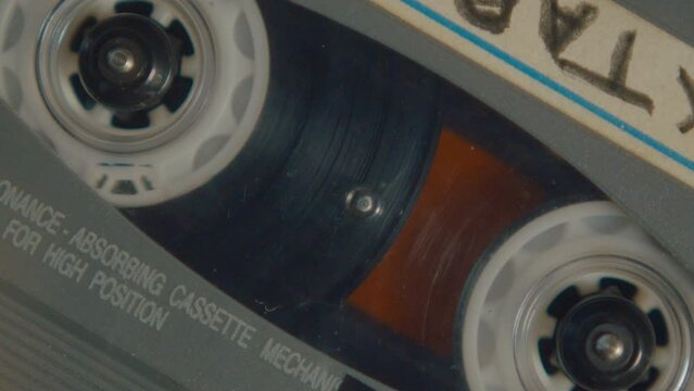 Extreme close-up view of reels on audio cassette tape turning while playing music