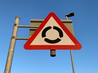 UK roundabout ahead warning sign against a clear blue sky, roundabout road sign