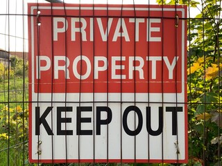 Red and white sign "private property Keep out" attached to a metal fence