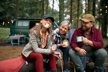 Teenage girl eats roast marshmallows while camping with parents in woods.
