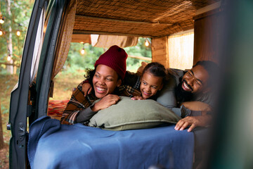 Cheerful black family relaxing in camping trailer in woods.