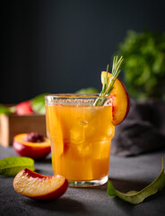 Peach tea with ice and rosemary on a glass. Vegan homemade healthy  drink on a dark background with fresh fruits close up. Rustic style.