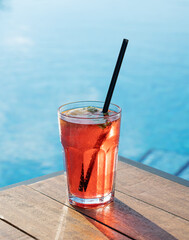 Fresh red berries mojito on a wooden tabletop in front of the pool. The concept of a summer refreshing drink on vacation.