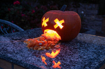 Funny puking Halloween pumpkin glowing with carved funny puking face with vomit and scary appearance in the darkness