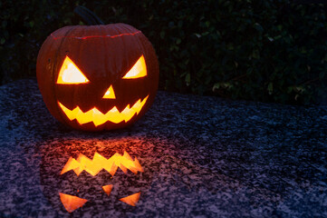 Homemade and internally illuminated glowing Halloween pumpkin with carved face and spooky appearance in the darkness