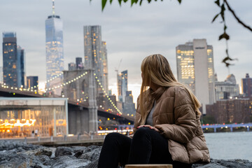 Fototapeta na wymiar travel woman sitting in the beach looking new york city building in sunset