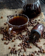 Coffee in a transparent cup, coffee beans, a transparent glass cezve and a manual coffee maker on an organic fabric on the table, morning, breakfast, photo in a dark key