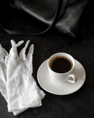 Coffee in a white cup, white gloves on a black table, morning, breakfast, dark photo