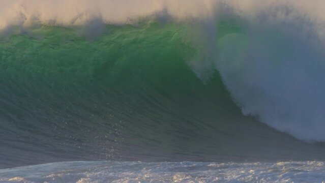 huge stormy wave breaking on a beach at sunset