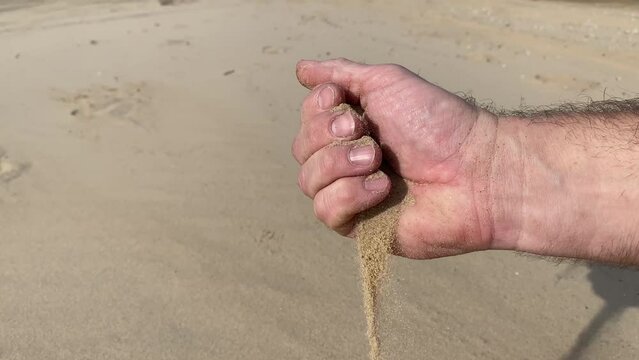 sand pours out through the fingers of a man's hand.