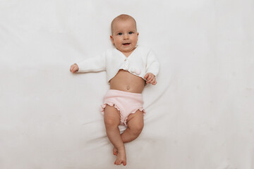 Funny newborn baby in a white knitted blouse and pink knitted underpants is lying on a white blanket. Copy space. 