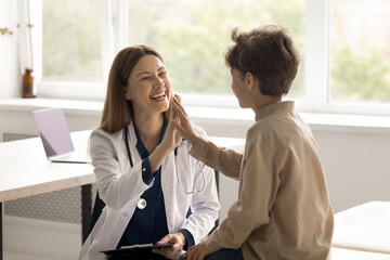 Happy little child boy patient giving high five to woman pediatrician in white uniform at consultation, celebrate successful treatment, finish meeting with friendly doctor. Good medical clinic service - obrazy, fototapety, plakaty
