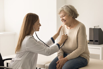 Cardiologist in coat examines older woman in clinic, listen to heartbeat with stethoscope during...