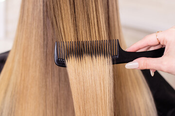 Fototapeta premium Hairdresser's hand brushing long natural blonde hair in beauty salon 