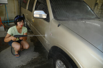 Pretty Asian woman Spraying water to wash the car.