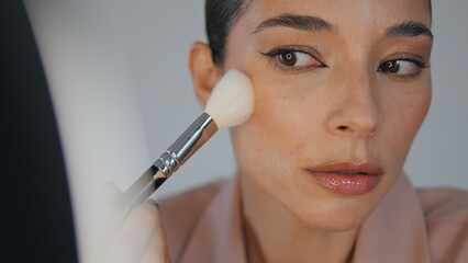 Closeup lady powdering face using brush home. Woman applying foundation makeup