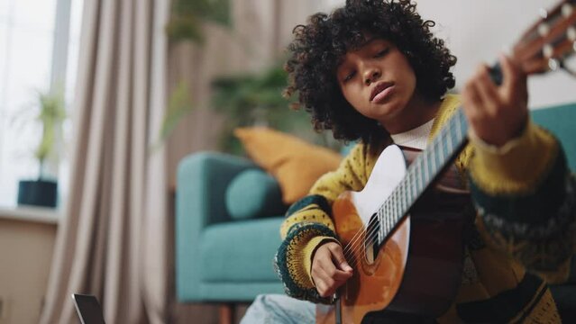 Online classes course guitar training African American girl playing guitar and watching online course on laptop while practicing at home Girl taking an online music class Education and science concept