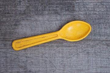one small dirty plastic spoon lies on a gray wooden table