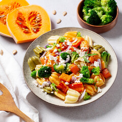 Autumn pasta salad with roasted pumpkin, broccoli, feta cheese on bright light background, fall season salad