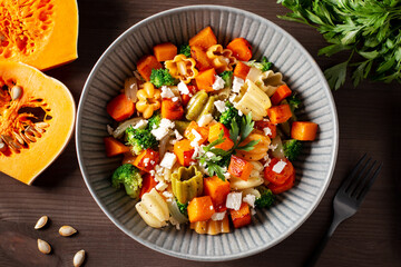 Autumn pasta salad with roasted pumpkin, broccoli, feta cheese on dark wooden background, fall season salad