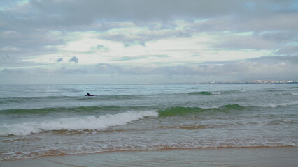 Surfer swimming ocean waves on cloudy day. Rolling sea water splashing hitting