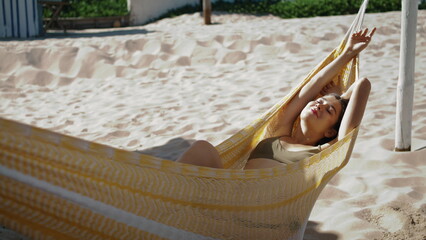 Fototapeta na wymiar Relaxed girl sunbathing hammock on sandy beach. Beautiful carefree woman resting