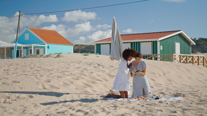 Lesbian couple using smartphone checking beach pictures. Two girls resting shore