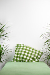 An empty bed with a green pillow and palm trees on the sides against a white wall. Place for text.