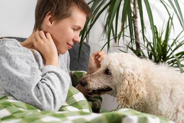 Throughout the day, a woman of middle age, her hair cut short, lounges in bed with her big poodle. Inactivity, weekend ease