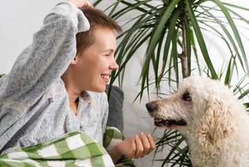 Throughout the day, a woman of middle age, her hair short, rests in bed with her large poodle. Inactivity, weekend ease