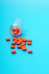 Red medicine pills scattered from glass bottle on blue background