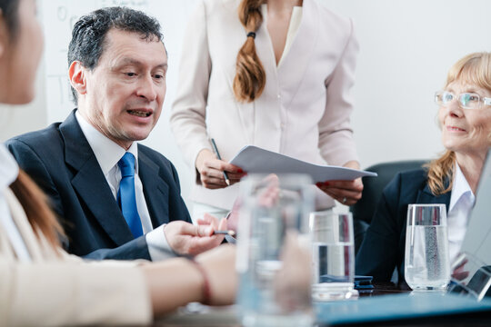 Side view of a Hispanic middle-aged skilled manager cooperating with his colleagues for finding solutions during a meeting in the conference room