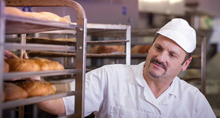 baker in a commercial bakery getting fresh bread out of the oven on trays