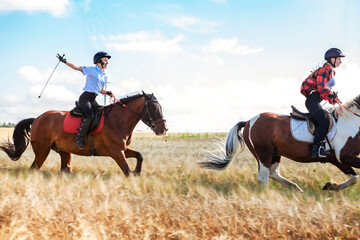 Young women equestrians gallop on horses through a field.
