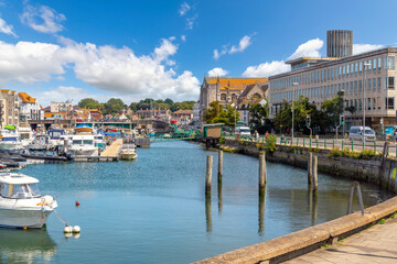 iew of the Weymouth Harbor, with boats docked in the marina, the Town Bridge, and the Holy Trinity St Nicholas Anglican Church, on a sunny summer day in Weymouth, England UK. - obrazy, fototapety, plakaty